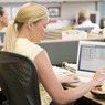 Businesswoman in cubicle using laptop and eating salad